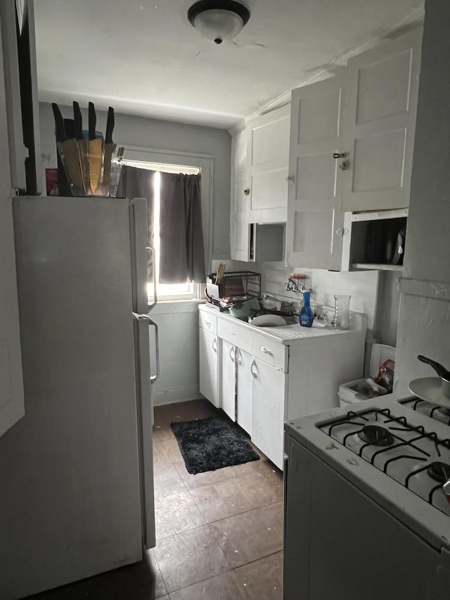 kitchen with sink, stainless steel fridge, decorative backsplash, white cabinets, and white gas range oven