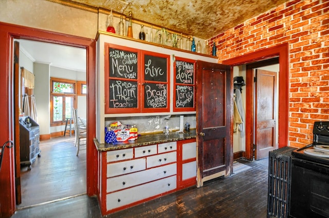 kitchen featuring backsplash, black range with electric stovetop, dark hardwood / wood-style floors, dark stone countertops, and brick wall