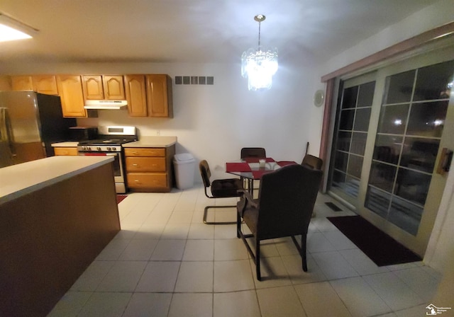 kitchen featuring light tile patterned flooring, black fridge, a chandelier, hanging light fixtures, and stainless steel range with gas cooktop