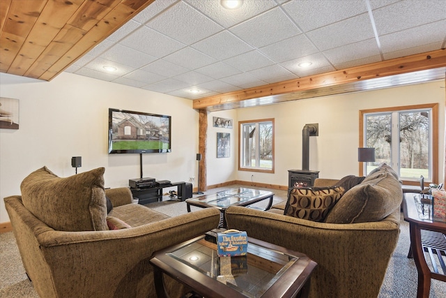 living room with carpet, a paneled ceiling, and a wood stove