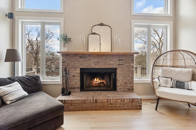 sitting room featuring wood-type flooring, a towering ceiling, a brick fireplace, and plenty of natural light