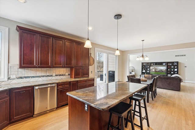 kitchen with a kitchen bar, light wood-type flooring, pendant lighting, dark stone countertops, and dishwasher