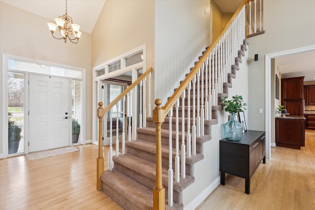 foyer entrance with high vaulted ceiling, light hardwood / wood-style flooring, and a notable chandelier