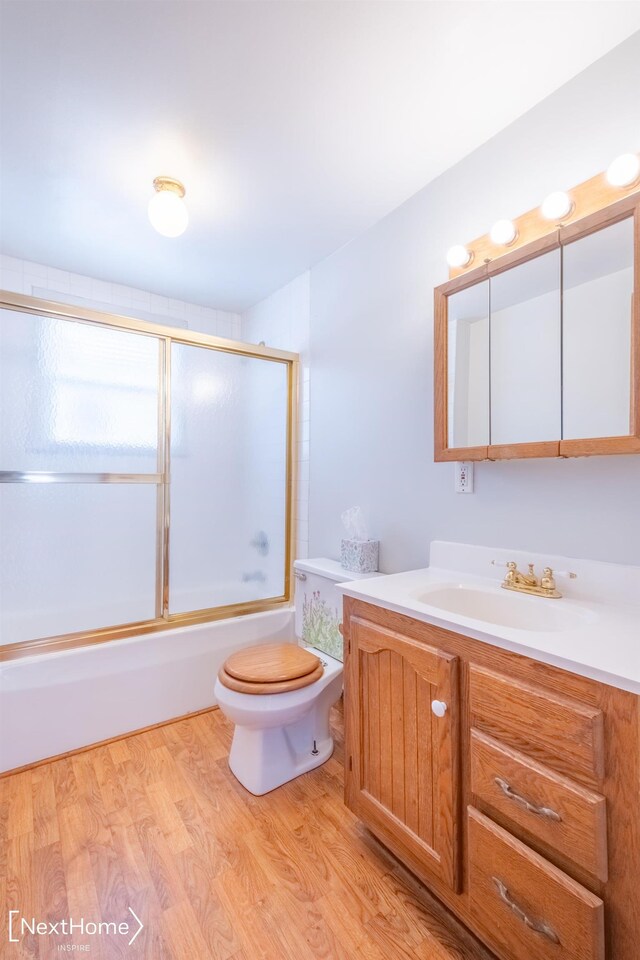 full bathroom with hardwood / wood-style floors, vanity, bath / shower combo with glass door, and toilet