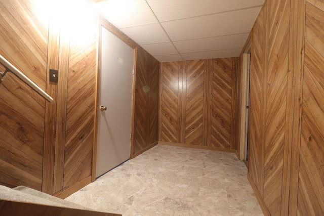 interior space with a drop ceiling and wood walls