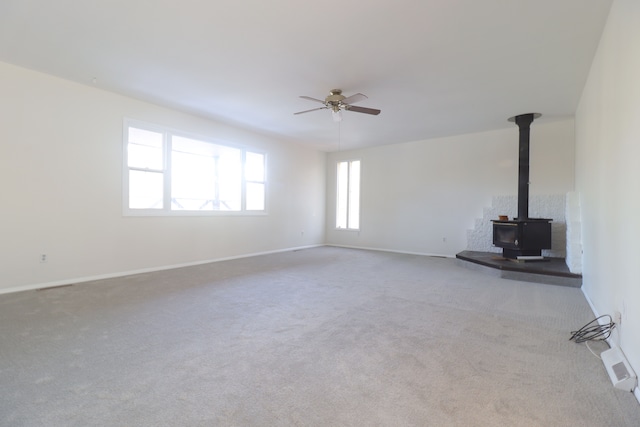 unfurnished living room featuring carpet flooring, a wood stove, and ceiling fan