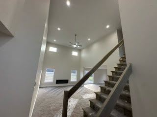 stairs with ceiling fan, carpet floors, and a high ceiling