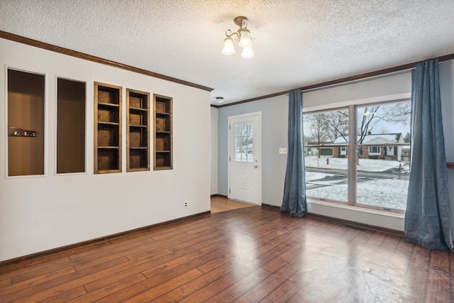 spare room featuring a textured ceiling, a wealth of natural light, crown molding, and dark hardwood / wood-style floors