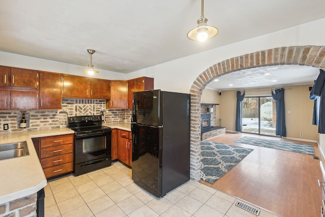 kitchen with sink, hanging light fixtures, tasteful backsplash, light hardwood / wood-style flooring, and black appliances