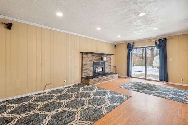 unfurnished living room featuring a textured ceiling, wooden walls, crown molding, wood-type flooring, and a wood stove