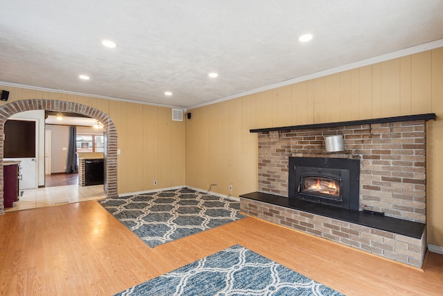 unfurnished living room with wooden walls, a fireplace, light hardwood / wood-style floors, and ornamental molding