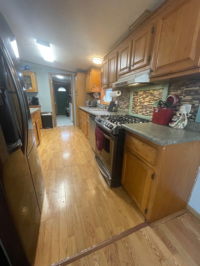 kitchen featuring sink, decorative backsplash, light hardwood / wood-style floors, stainless steel appliances, and a textured ceiling