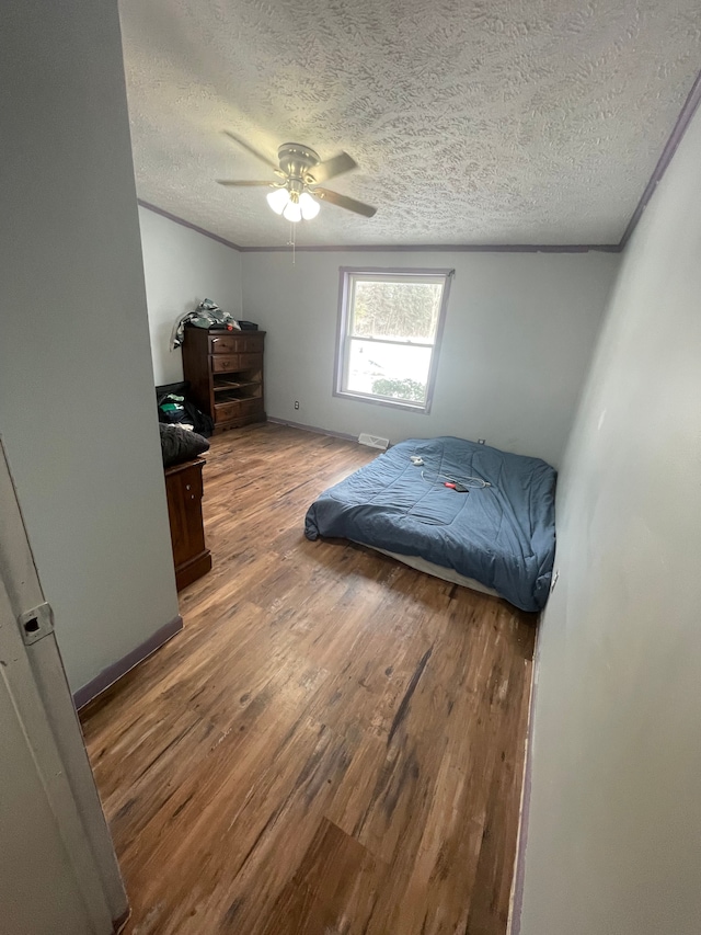 bedroom with ceiling fan, wood-type flooring, ornamental molding, and a textured ceiling