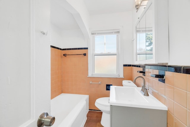 bathroom featuring vanity, a tub to relax in, toilet, and tile walls