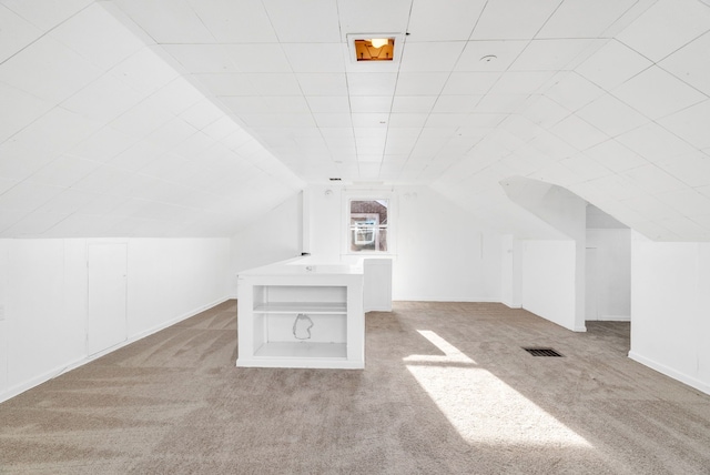 additional living space featuring built in shelves, light colored carpet, and vaulted ceiling