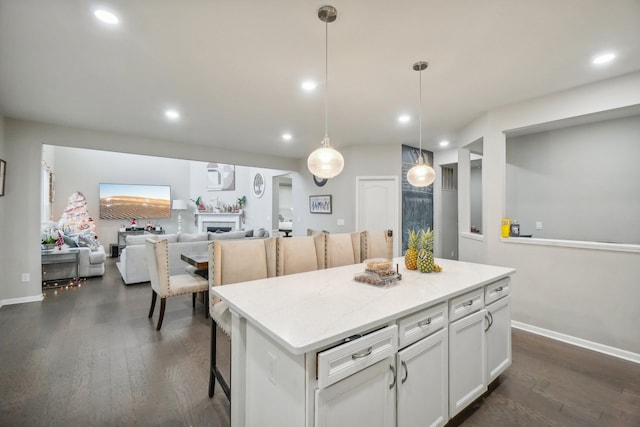 kitchen featuring a kitchen island, light stone counters, dark hardwood / wood-style flooring, pendant lighting, and white cabinets