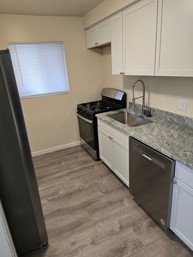 kitchen with appliances with stainless steel finishes, white cabinetry, sink, light wood-type flooring, and light stone counters