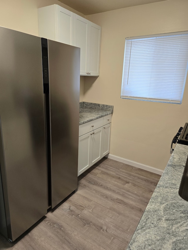 kitchen with white cabinets, stainless steel refrigerator, light stone counters, light hardwood / wood-style flooring, and stove