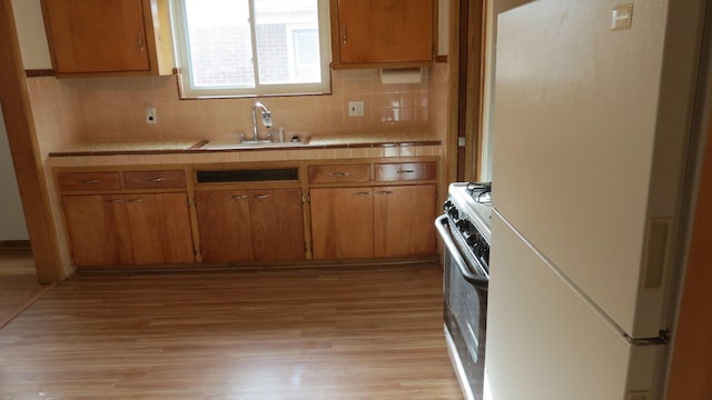 kitchen featuring tile counters, sink, light hardwood / wood-style flooring, white appliances, and decorative backsplash