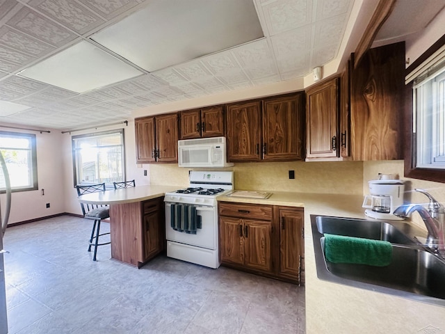 kitchen featuring kitchen peninsula, sink, white appliances, and a breakfast bar area