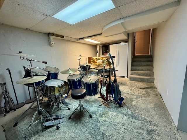 basement with a paneled ceiling and white refrigerator with ice dispenser