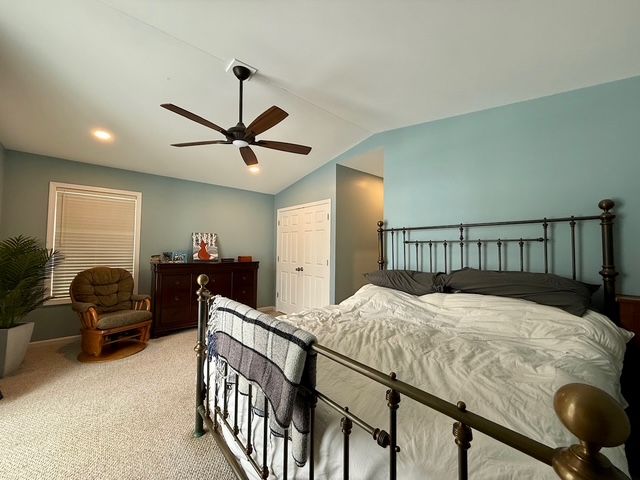 carpeted bedroom with ceiling fan, a closet, and vaulted ceiling