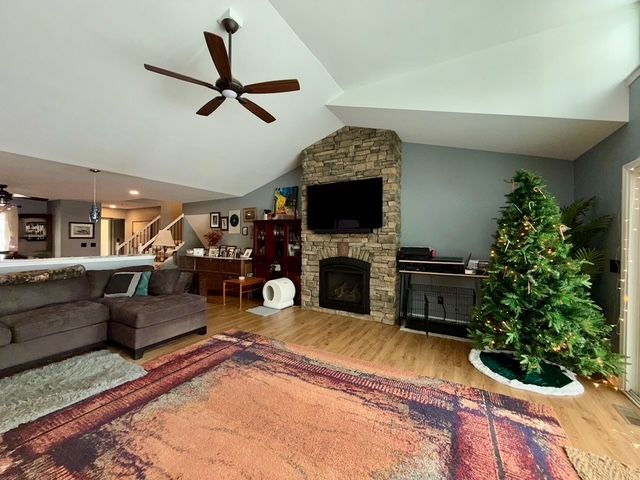 living room with ceiling fan, a stone fireplace, wood-type flooring, and lofted ceiling