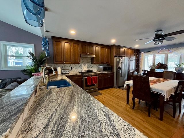 9471 Ridge Rd, Goodrich, MI 48438 - kitchen with a sink, stainless steel appliances, under cabinet range hood, stone counters, and light wood-style floors