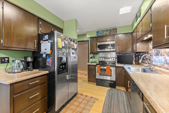 kitchen with dark brown cabinetry, sink, stainless steel appliances, tasteful backsplash, and light hardwood / wood-style flooring