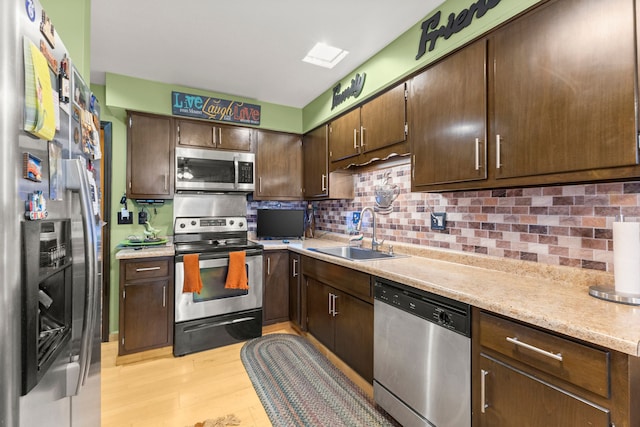 kitchen with appliances with stainless steel finishes, backsplash, dark brown cabinets, sink, and light hardwood / wood-style flooring