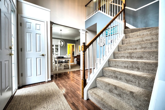 foyer entrance with a notable chandelier, dark hardwood / wood-style flooring, ornate columns, and ornamental molding