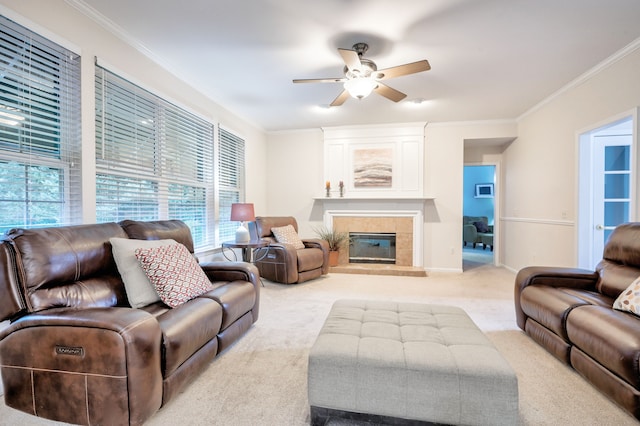 living room featuring a tile fireplace, light colored carpet, ceiling fan, and crown molding