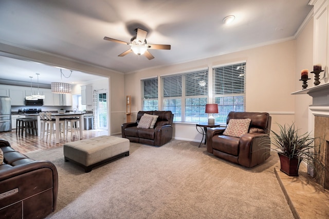 living room featuring a tile fireplace, crown molding, ceiling fan, and light colored carpet