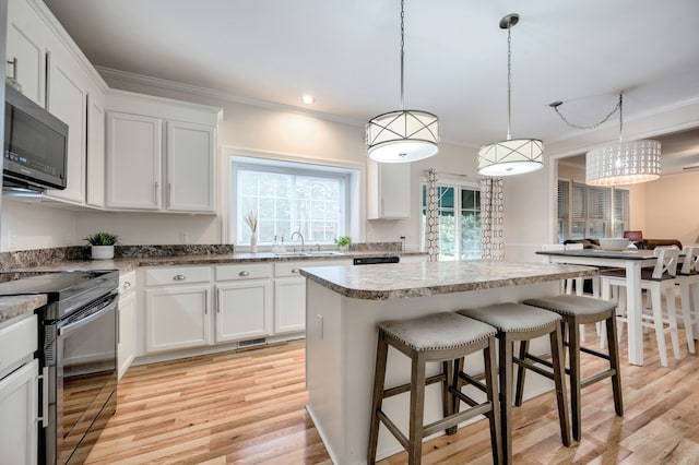 kitchen with white cabinets, light hardwood / wood-style floors, appliances with stainless steel finishes, decorative light fixtures, and a kitchen island