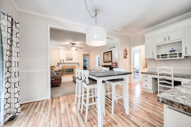 dining space featuring crown molding, ceiling fan, built in desk, and light hardwood / wood-style floors