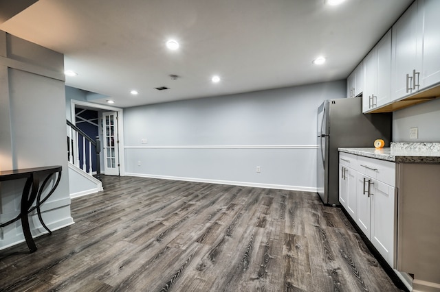 kitchen with stainless steel refrigerator, light stone counters, white cabinets, and dark hardwood / wood-style floors