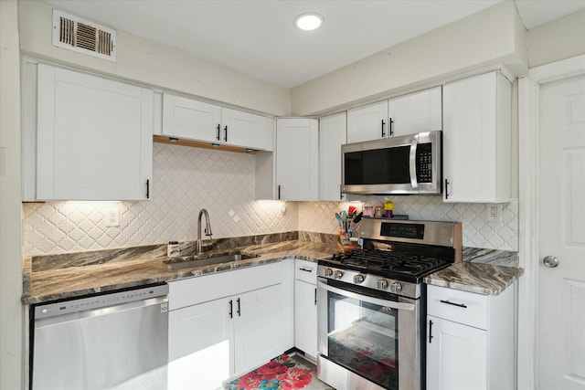 kitchen with tasteful backsplash, white cabinetry, sink, dark stone countertops, and stainless steel appliances