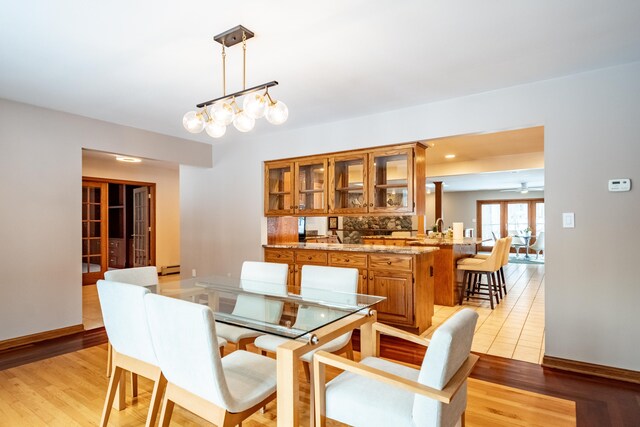 dining room featuring ceiling fan with notable chandelier, a baseboard heating unit, french doors, and light hardwood / wood-style flooring