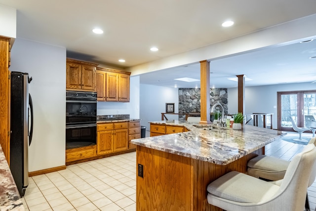 kitchen with sink, black double oven, ornate columns, a kitchen bar, and stainless steel refrigerator