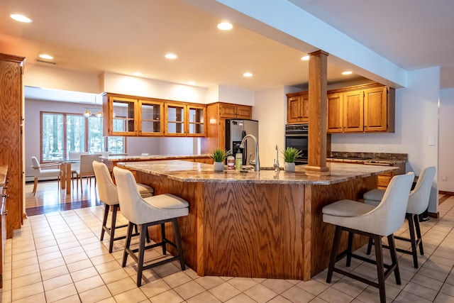 kitchen featuring stainless steel fridge, a kitchen breakfast bar, a large island with sink, and dark stone countertops