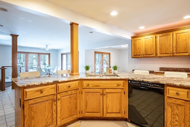 kitchen with light tile patterned floors, black dishwasher, light stone counters, decorative columns, and a sink