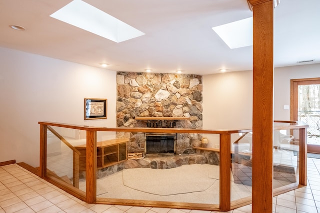 living area with a stone fireplace, tile patterned flooring, visible vents, and a skylight