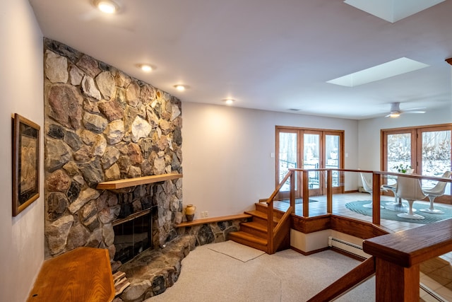 living room featuring a skylight, ceiling fan, a baseboard radiator, a fireplace, and carpet floors