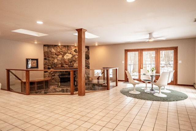 living room with a skylight, a stone fireplace, ceiling fan, and decorative columns