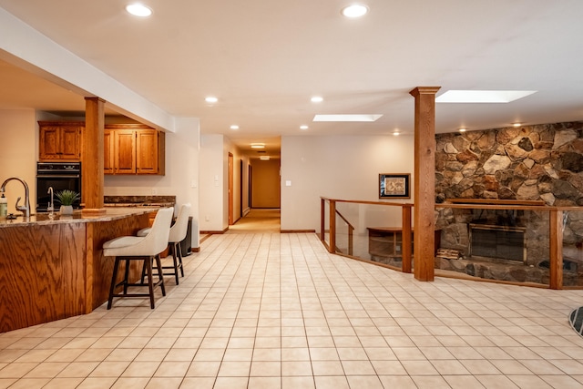 kitchen with sink, a kitchen breakfast bar, a stone fireplace, double oven, and stone countertops