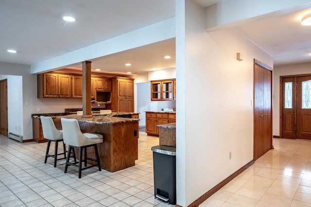 kitchen with a breakfast bar, baseboard heating, light tile patterned floors, dark stone countertops, and a kitchen island