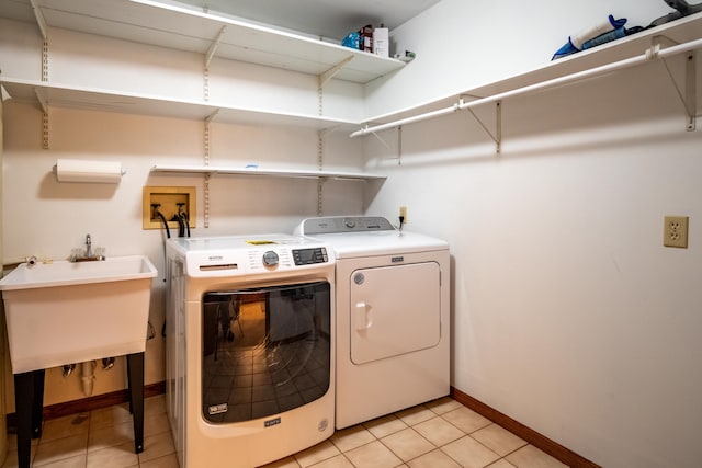 washroom with light tile patterned floors, a sink, laundry area, washer and clothes dryer, and baseboards