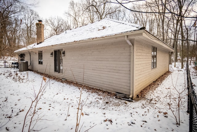 view of snow covered exterior featuring central AC, metal roof, and a chimney