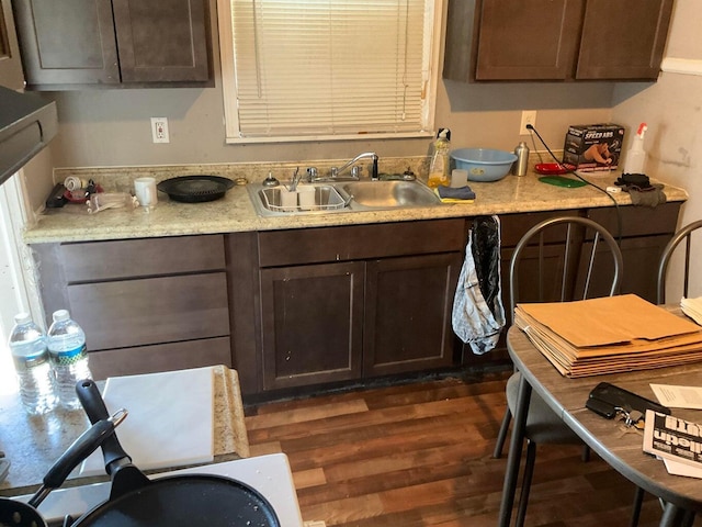 kitchen with light stone countertops, dark hardwood / wood-style flooring, dark brown cabinetry, and sink