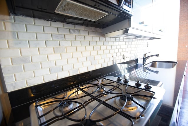 room details featuring cooktop, tasteful backsplash, range hood, and sink